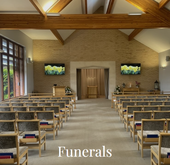 Photograph of an empty chapel that is set up for a funeral. There are wooden chairs on each side of the isle, and a catafalque at the end. Clicking on this photo will take you to the Funerals page of the website.